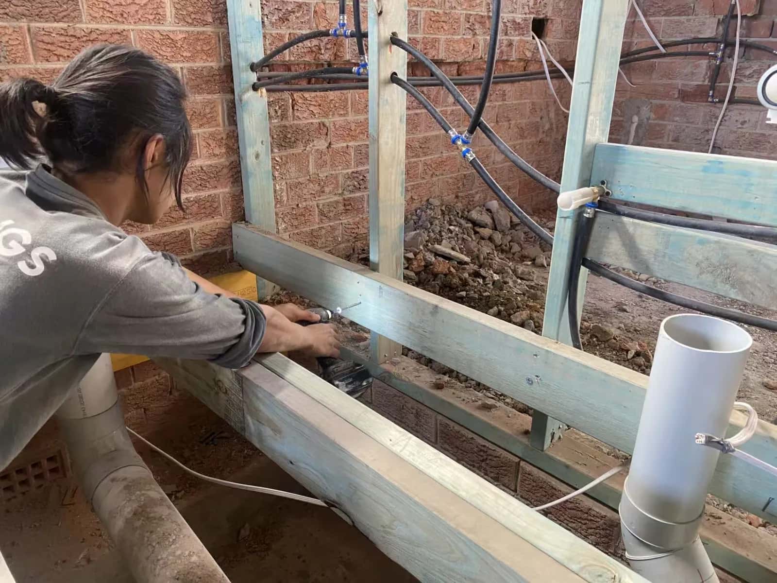 Worker fitting timber floor framing beside exposed brickwork and pipework at the Turramurra renovation