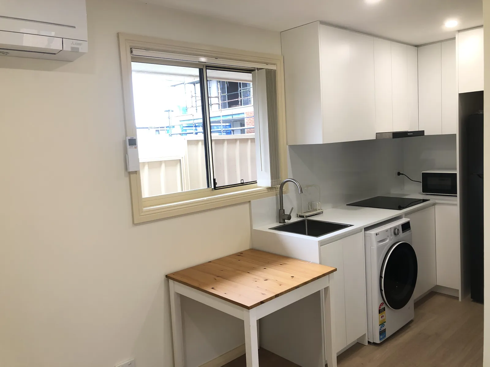 Completed Eastwood kitchenette with white cabinetry, black sink, glass splashback and laundry appliance
