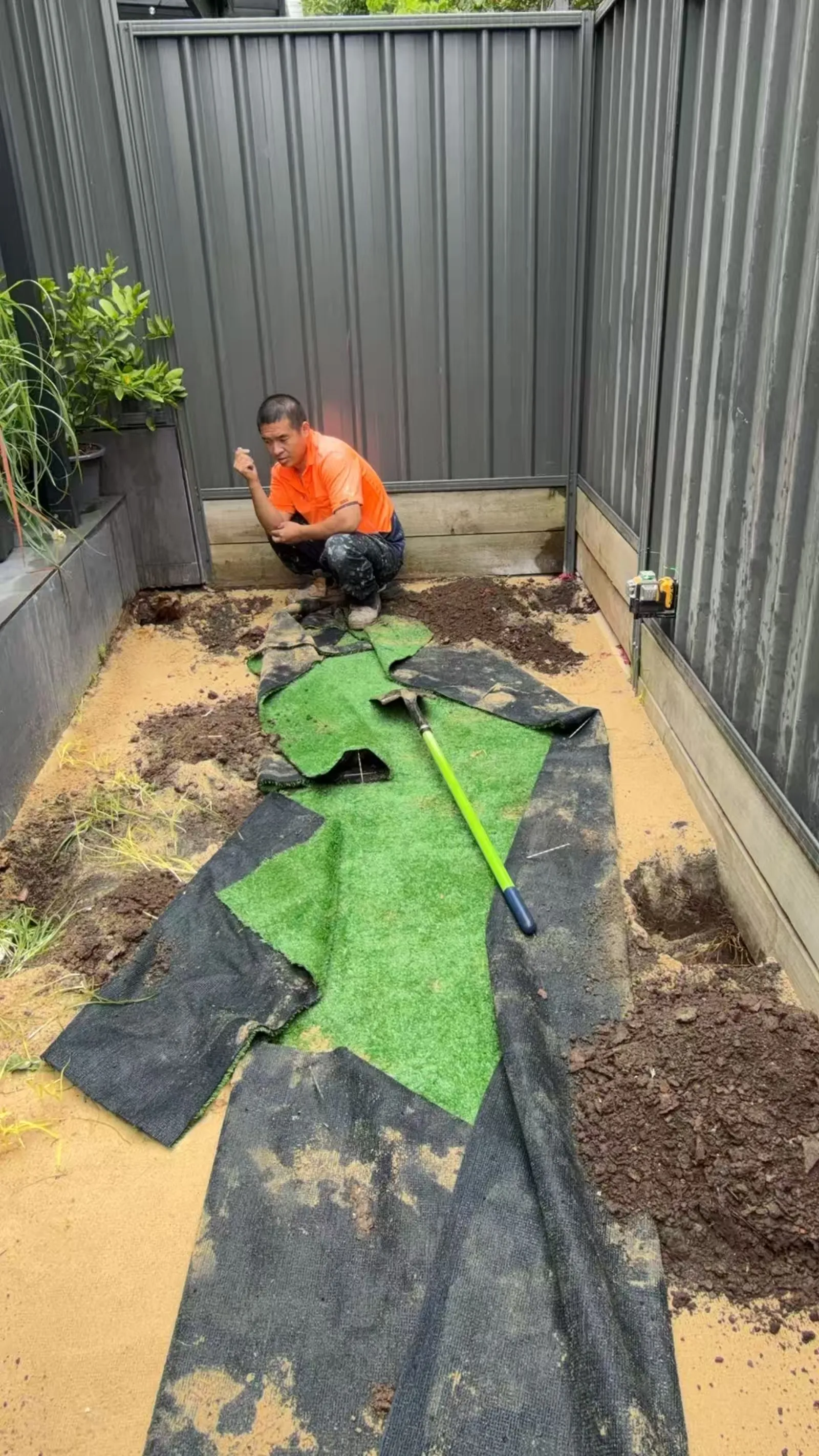 Worker preparing the ground in a fenced Dundas courtyard during the deck project