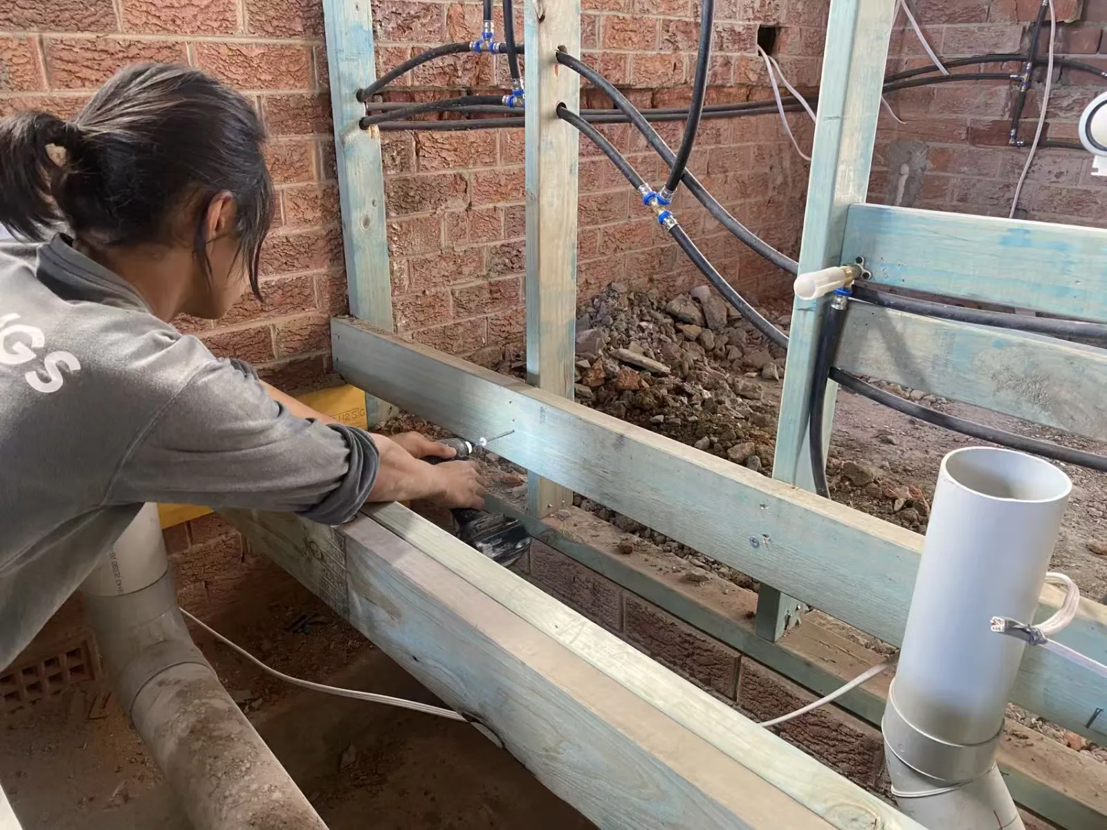Worker fitting timber floor framing beside exposed brickwork and pipework at the Turramurra renovation