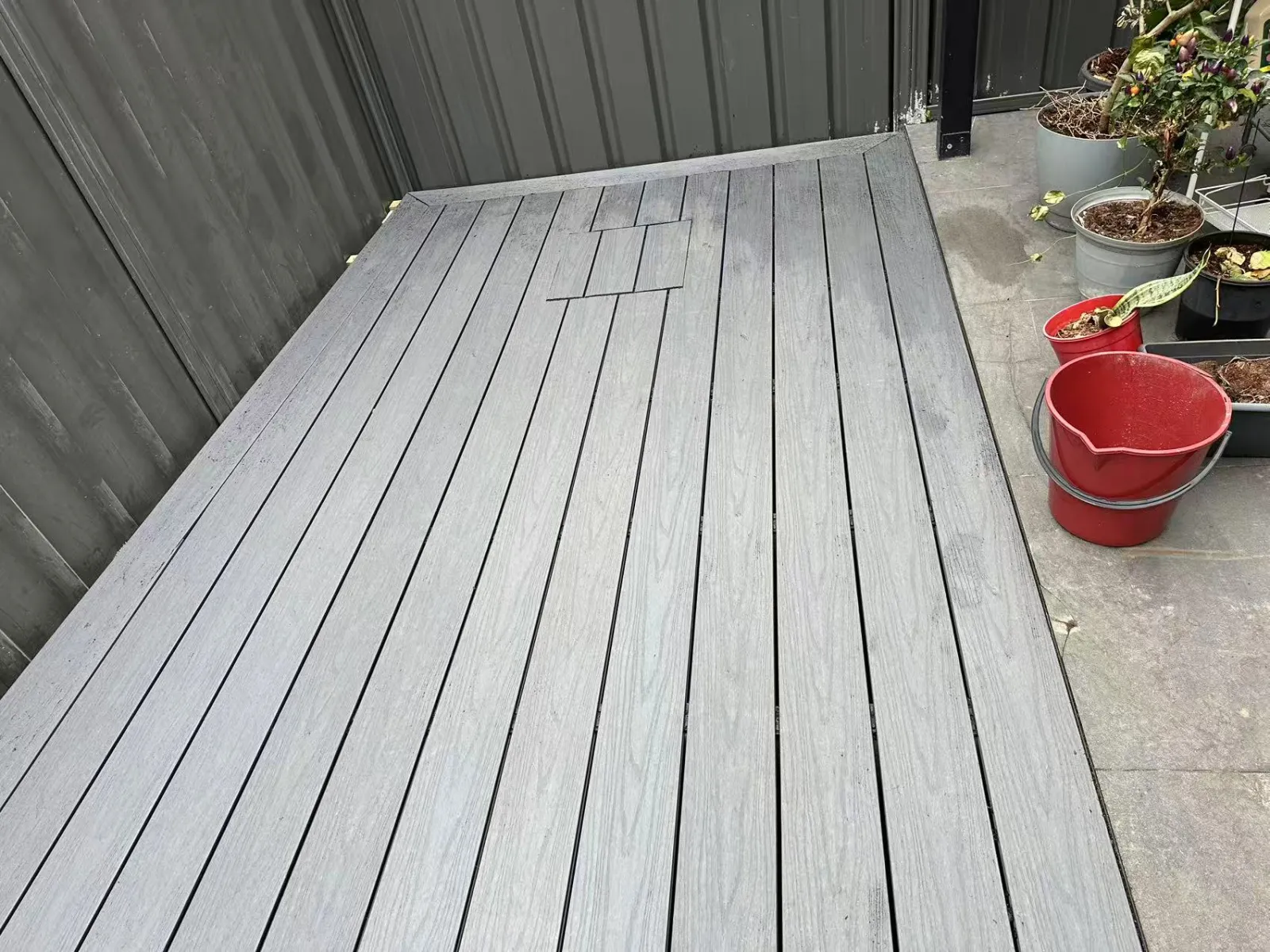 Completed grey deck in a Dundas courtyard, beside metal fencing and pot plants